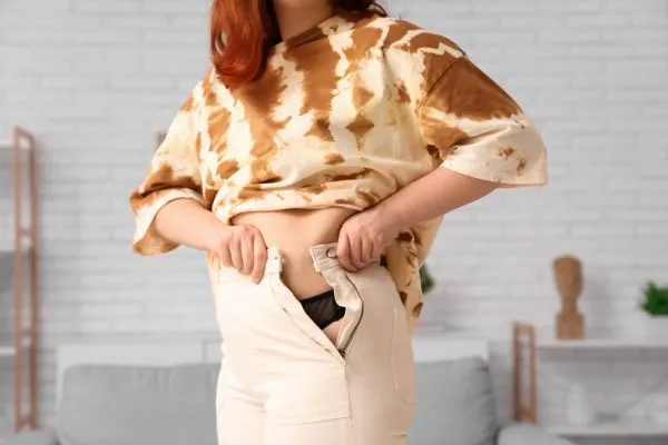 Image of woman trying to do her trousers up after pregnancy weight gain Benson