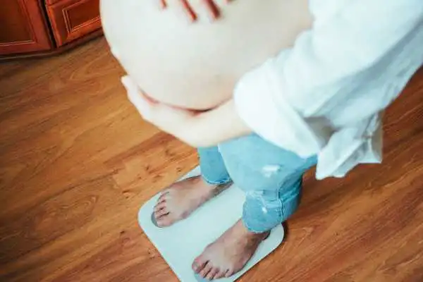 Image of woman weighing herself and experiencing weight gain through pregnancy Benson